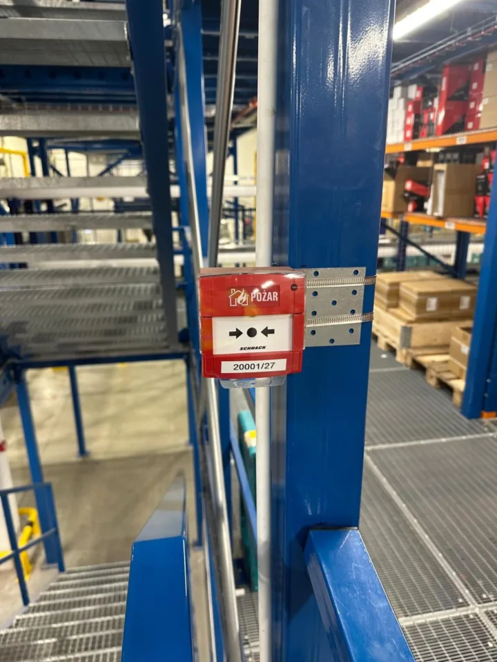 Ręczny ostrzegacz pożarowy zainstalowany na konstrukcji stalowej regałów magazynowych jako część systemu sygnalizacji pożaru