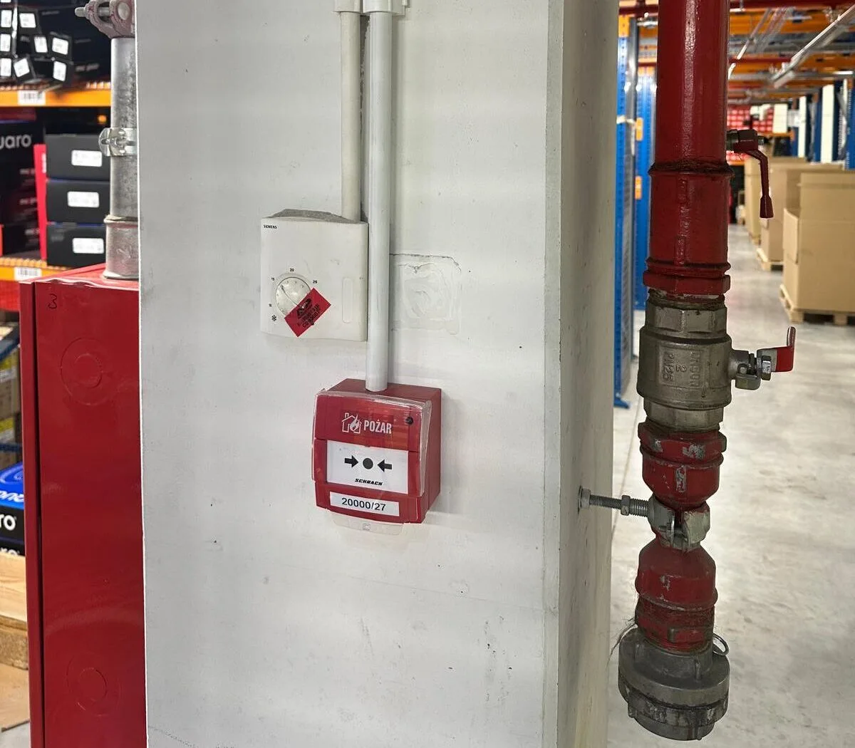 Ręczny ostrzegacz pożarowy ROP zamontowany na ścianie magazynu, obok instalacji tryskaczowej i prowadzenia instalacji SSP