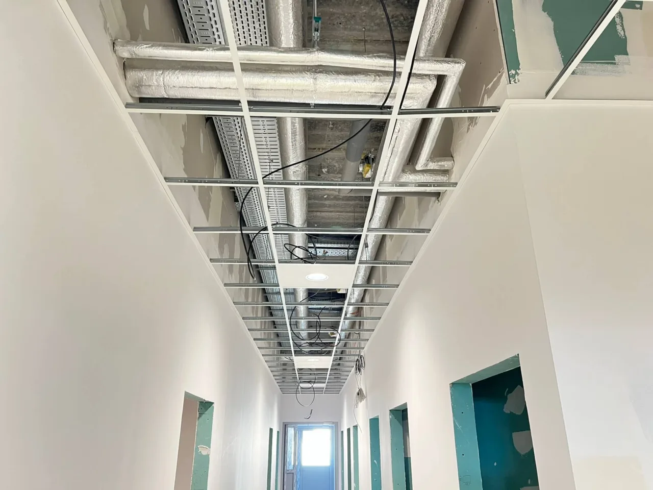 Korytarz w trakcie prac wykończeniowych – montaż instalacji w przestrzeni sufitu podwieszanego w budynku Karmello