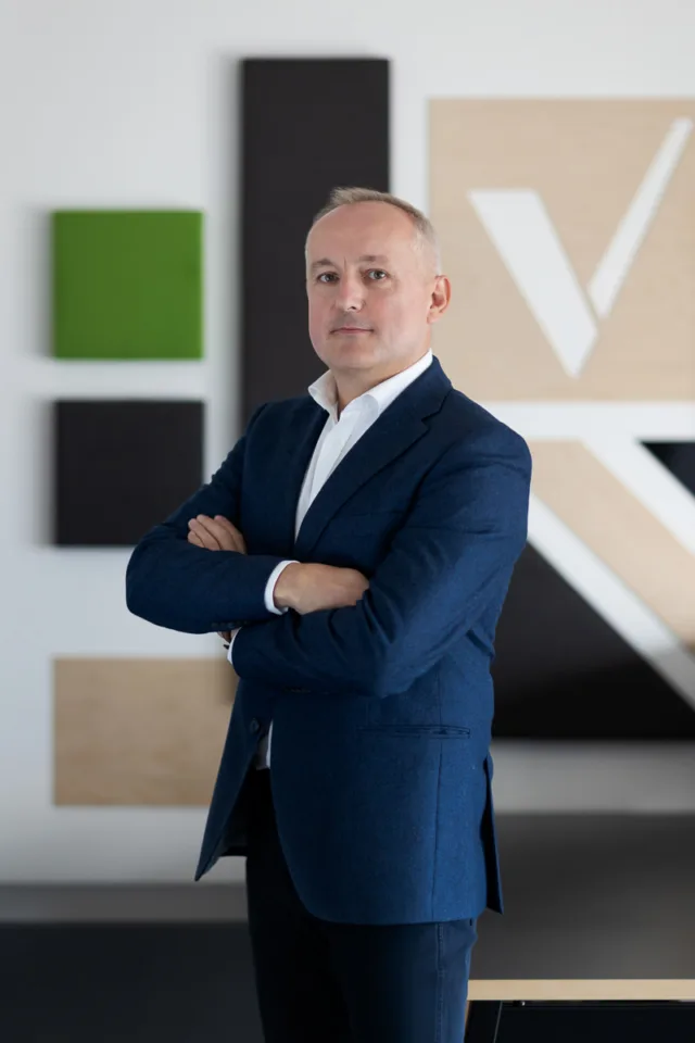 Tomasz Kowalski, Prezes Zarządu VSYSTEM, na tle elementów identyfikacji wizualnej firmy.